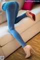 A woman in blue jeans and high heels is sitting on a couch.