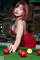 A woman in a red dress playing pool.