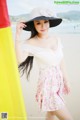 A woman in a white dress and a black hat on the beach.