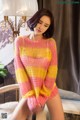 A woman in a pink and yellow sweater sitting on a chair.