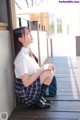 A woman in a school uniform sitting on a wooden floor.