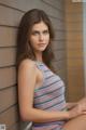 A woman in a striped tank top leaning against a wall.