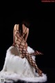 A woman in a black bodystocking sitting on a white fur rug.