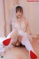 A woman in a wedding dress and red shoes sitting on the floor.