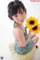 A young woman sitting on a pillow holding a sunflower.